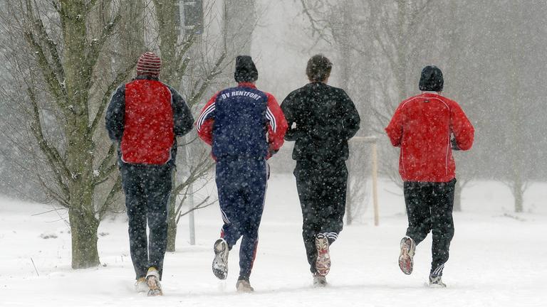 Vier Männer joggen nebeneinander über einen verschneiten Weg.