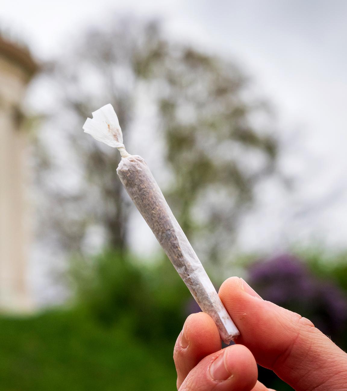 Ein Mann hält einen Joint vor der Kulisse des Monopteros im Englischen Garten