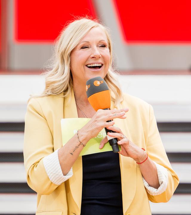 Andrea Kiewel steht vor der Kamera im Fernsehgarten