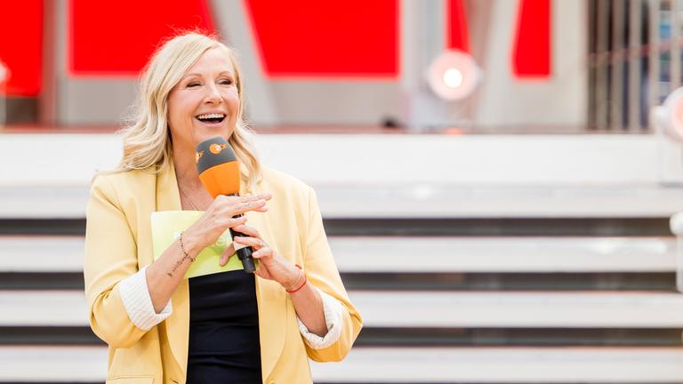 Andrea Kiewel steht vor der Kamera im Fernsehgarten