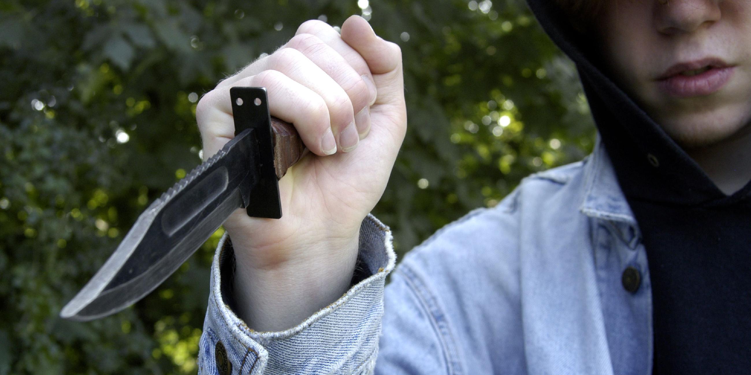 Ein Jugendlicher mit Kapuze hält ein Messer in der Hand.