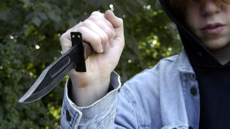 Ein Jugendlicher mit Kapuze hält ein Messer in der Hand.