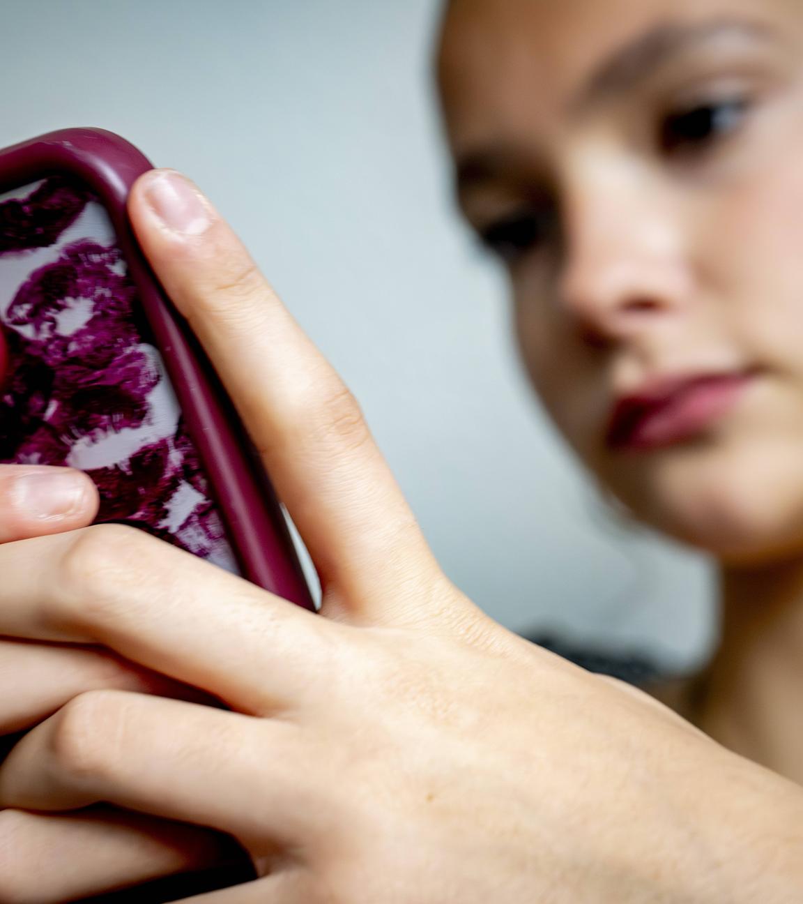 Eine Jugendliche sitzt vor ihrem Smartphone und blickt auf den Bildschirm.