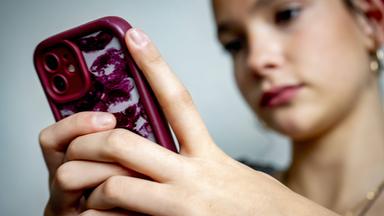 Eine Jugendliche sitzt vor ihrem Smartphone und blickt auf den Bildschirm.