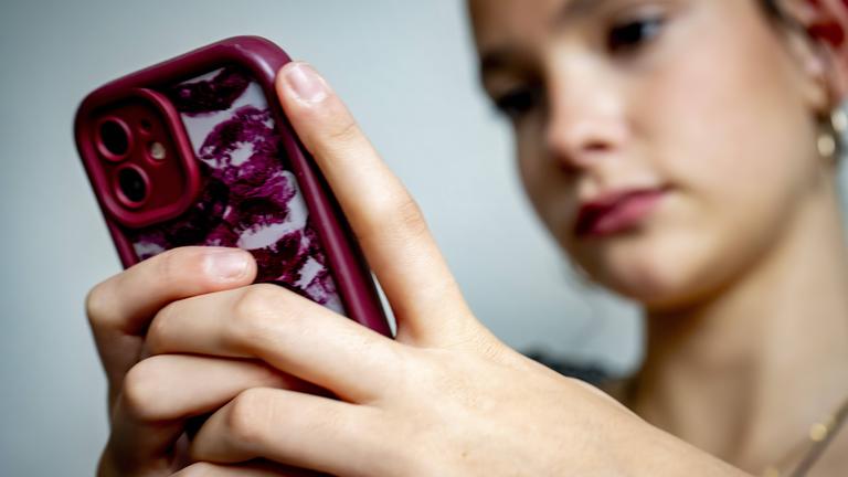 Eine Jugendliche sitzt vor ihrem Smartphone und blickt auf den Bildschirm.