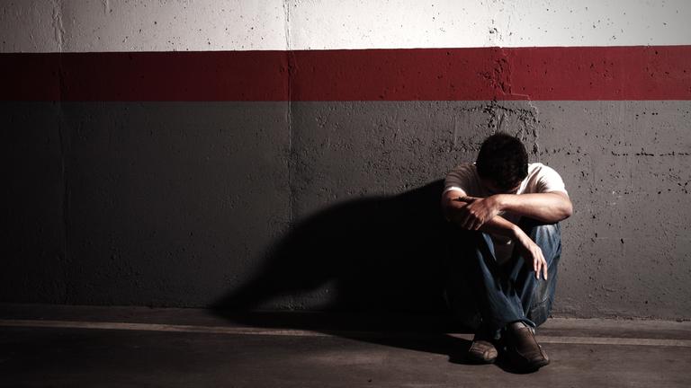 Jugendlicher sitzt traurig an der Wand.