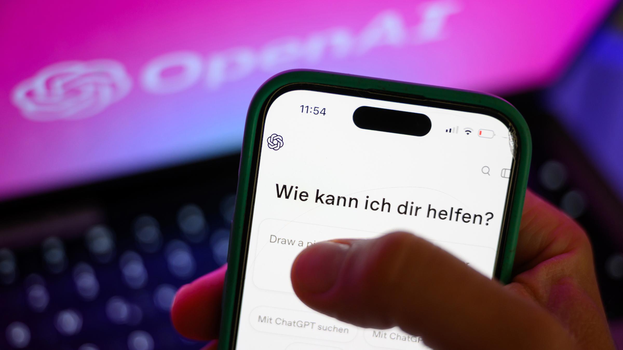 Ein Smartphone mit dem KI-Chatbot ChatGPT ist vor dem Logo des US-Softwareunternehmens OpenAI zu sehen