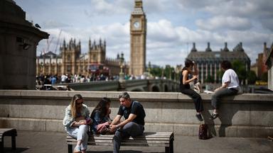 Im Vordergrund sind junge Menschen, die auf einer Bank sitzen. Im Hintergrund ist die Stadt London zu sehen.
