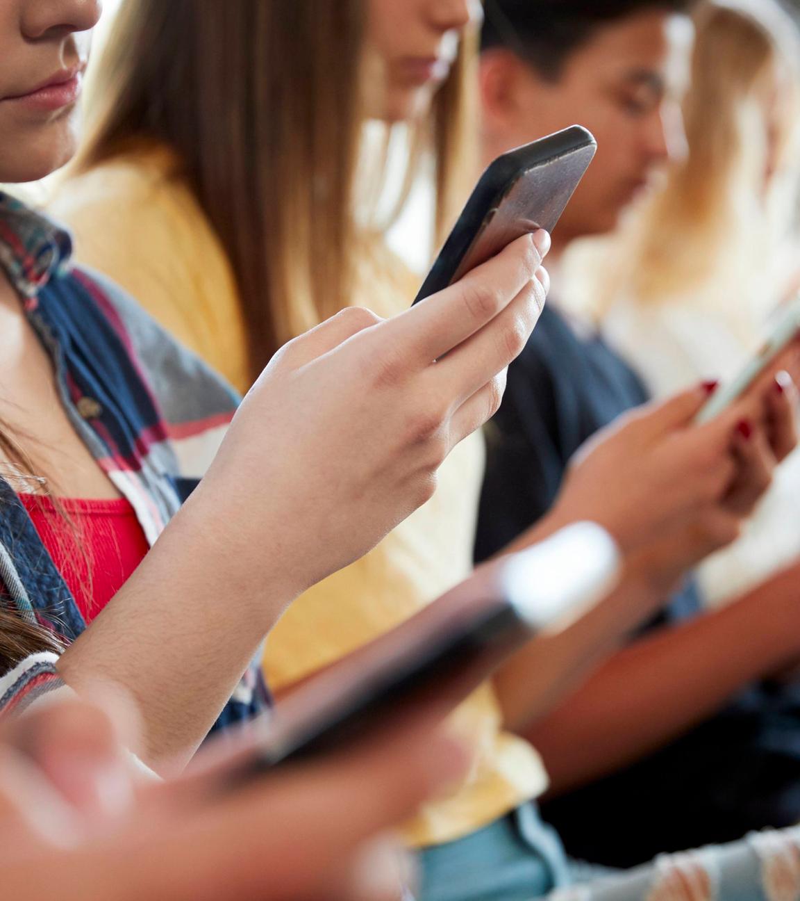 Eine Gruppe Jugendlicher sitzt nebeneinander und schaut auf Smartphone.
