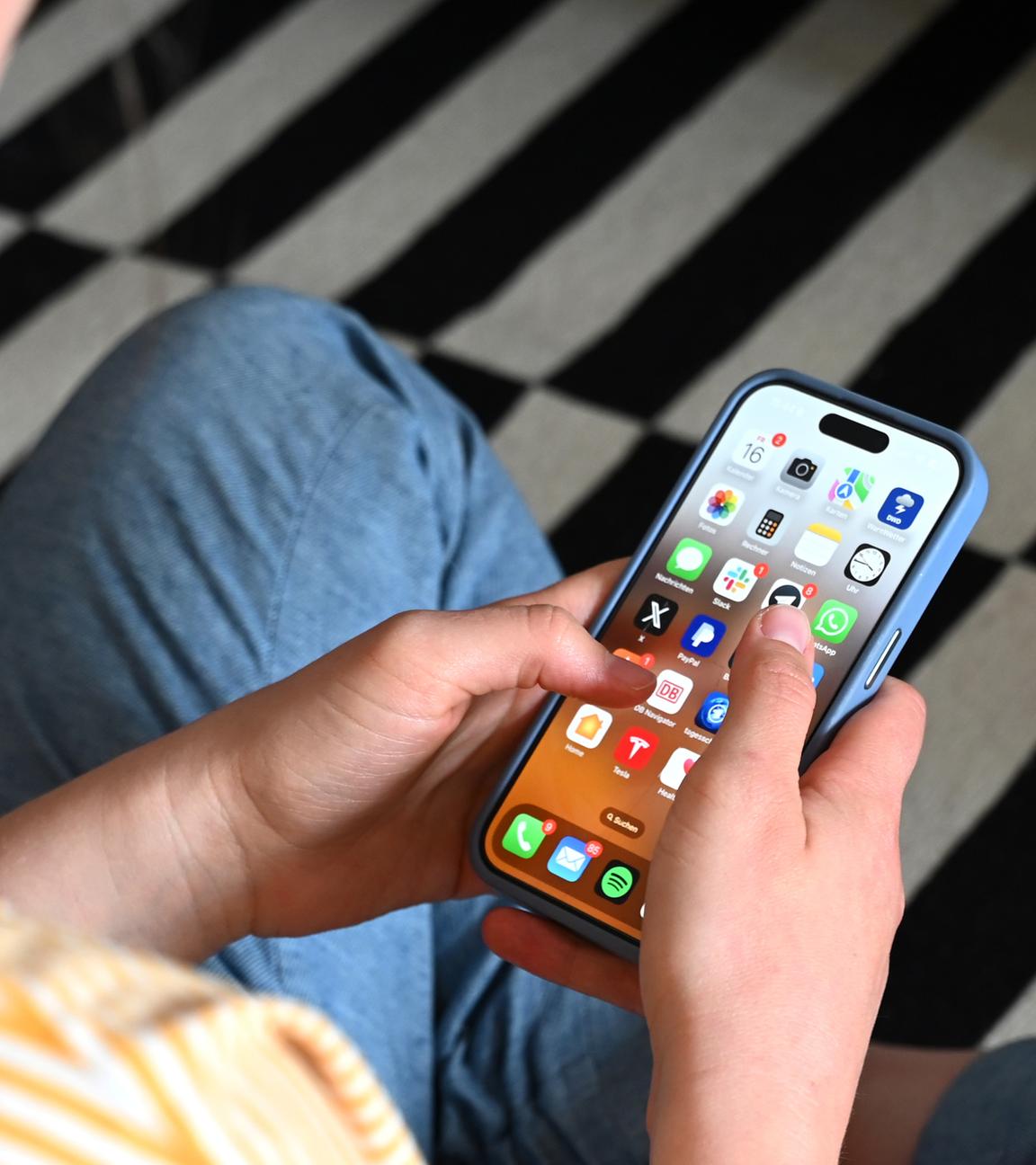 Eine Jugendliche sitzt auf dem Boden und nutzt ein Smartphone - auf dem Display sind verschiedene Apps zu sehen.