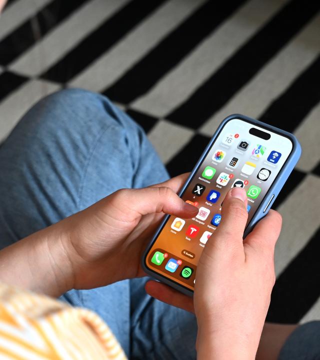 Eine Jugendliche sitzt auf dem Boden und nutzt ein Smartphone - auf dem Display sind verschiedene Apps zu sehen.