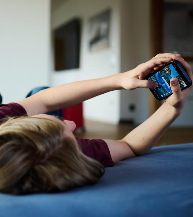 Ein Teenager guckt auf ein Handy, während er auf einer Matratze liegt. 