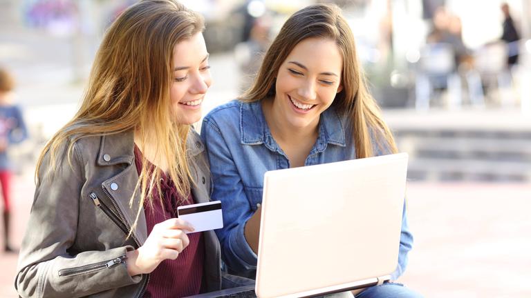 Zwei Jugendliche sitzen vor einem Laptop. Ein Mädchen hat einen Bankkarte in der Hand.