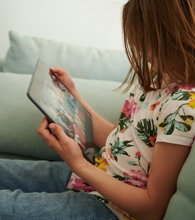 Berlin: Ein Mädchen sitzt auf der Couch und guckt in das Tablet ihrer Eltern.