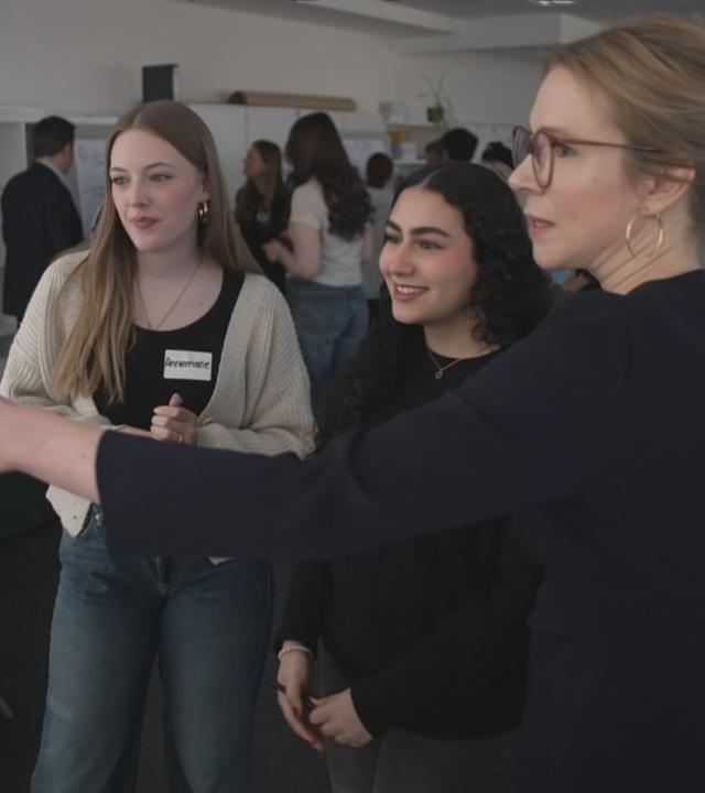Eine ältere und zwei jüngere Frauen vor einem Whiteboard