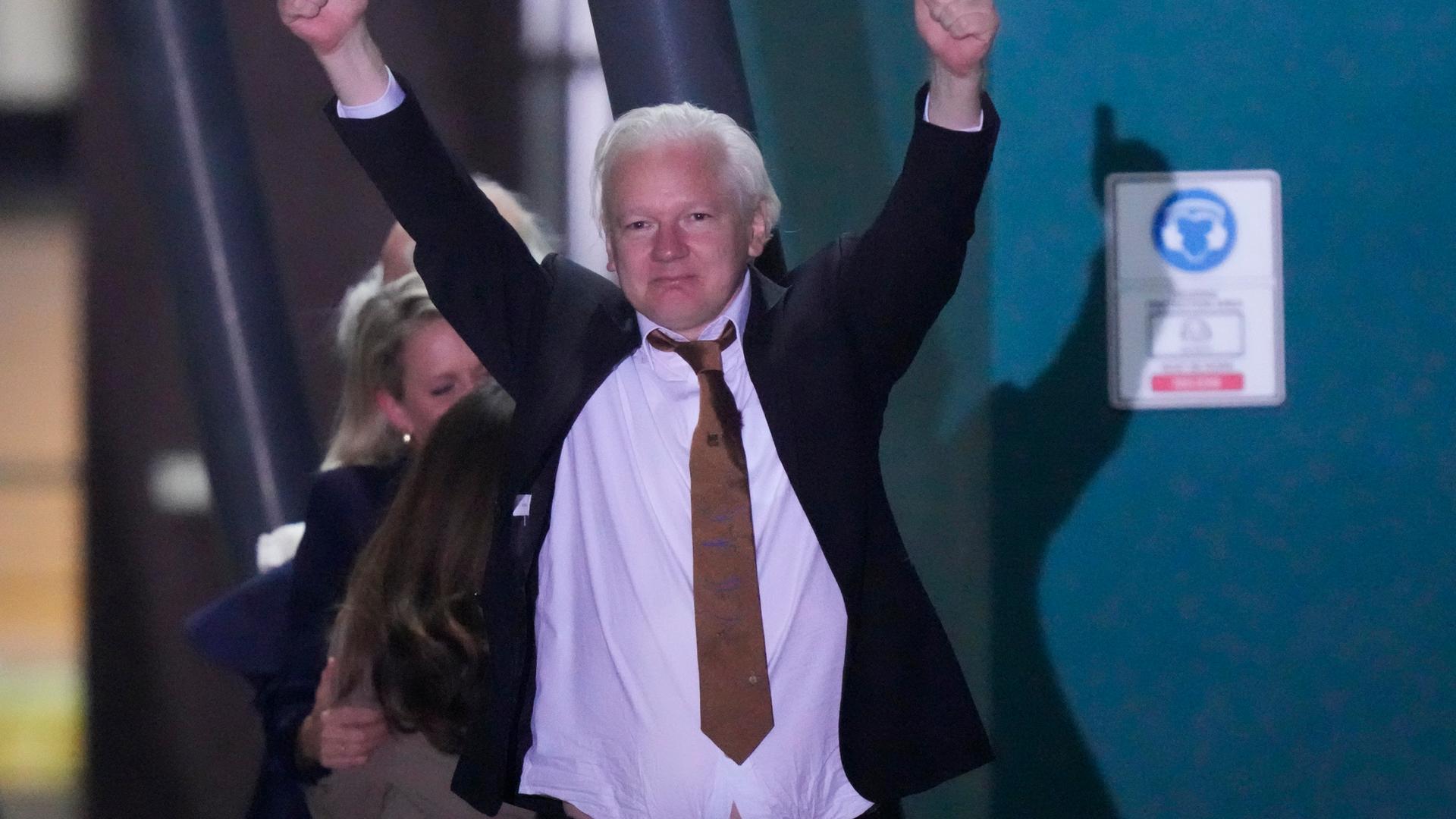 Julian Assange streckt seine Arme noch oben und zeigt zwei Daumen nach oben.