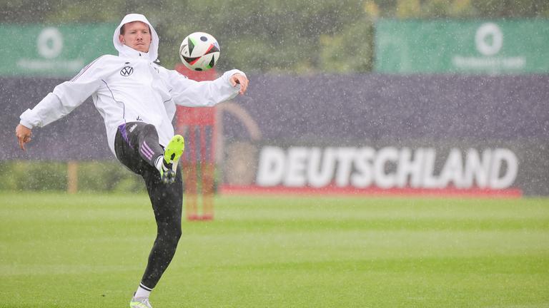 Deutschlands Trainer Julian Nagelsmann spielt einen Ball zu Beginn des Trainings im strömenden Regen. 