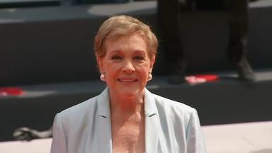 Julie Andrews bei einer öffentlichen Veranstaltung, aufgenommen in einer Nahaufnahme. Sie trägt einen hellen Blazer und runde Ohrringe; der Hintergrund ist unscharf.