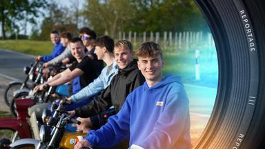 "ZDF.reportage: Jung im Osten – Wie wir wirklich leben": Jason aus Flurstedt und andere Jugendliche sitzen auf Simson-Mopeds und lächeln in die Kamera. Im Hintergrund verläuft eine schmale Landstraße, an der Bäume stehen.