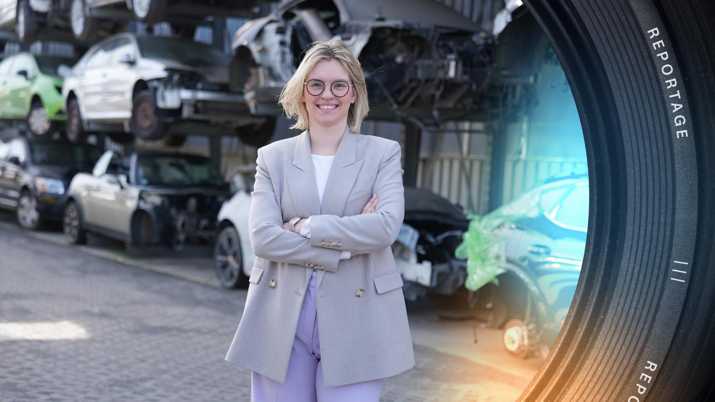 Chefin Anne-Marie Bender steht mit verschränkten Armen vor gestapelten Autos auf dem Hof ihres Recyclingbetriebes.