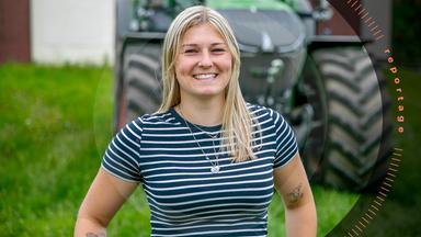 Lucy Schmidt steht lachend vor einem Traktor.