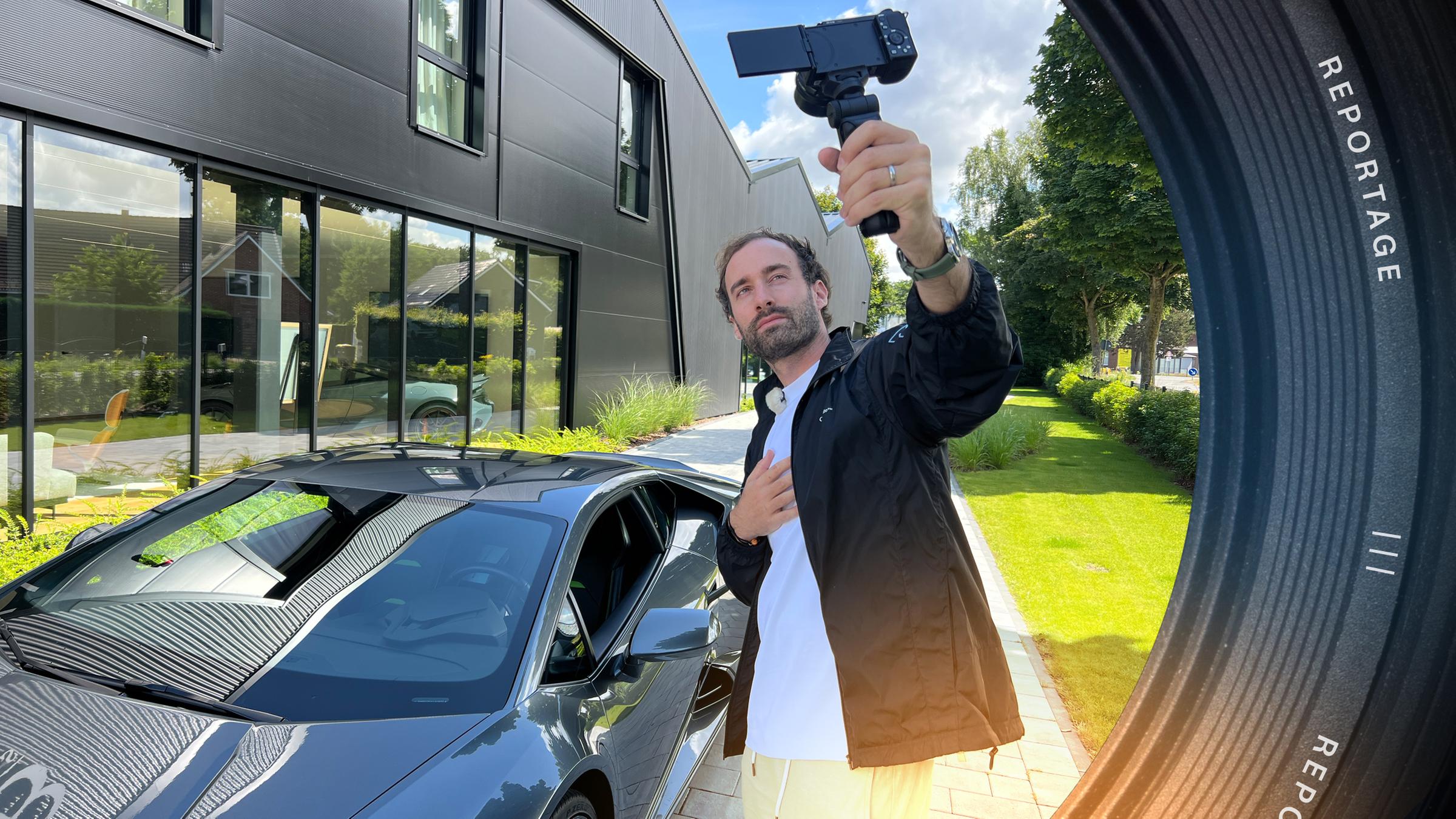 Ein junger Mann hält eine Handykamera hoch und filmt sich mit einem Lamborghini.