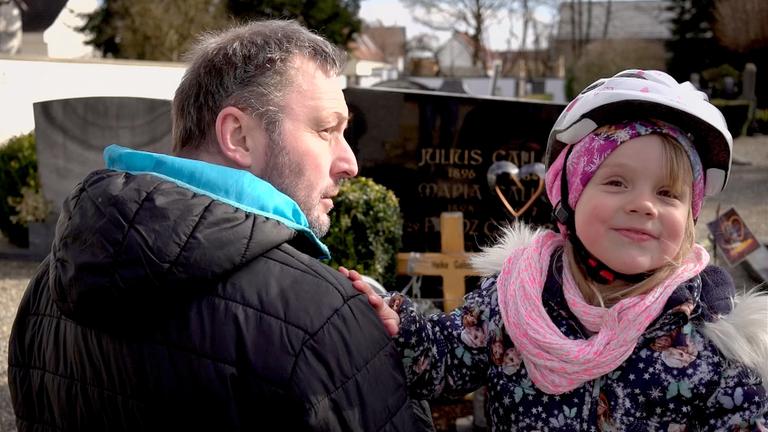 Stephan ist mit seiner dreijährigen Tochter Greta mit Fahrradhelm auf dem Friedhof.