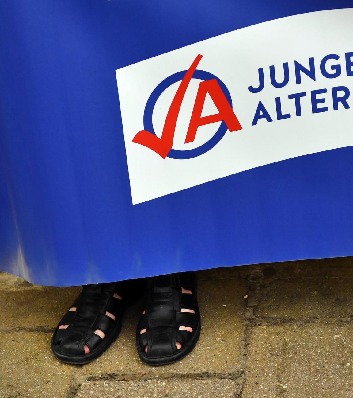 Ein Mann in schwarzen Sandalen hält ein Plakat der AfD-Jugendorganisation Junge Alternative