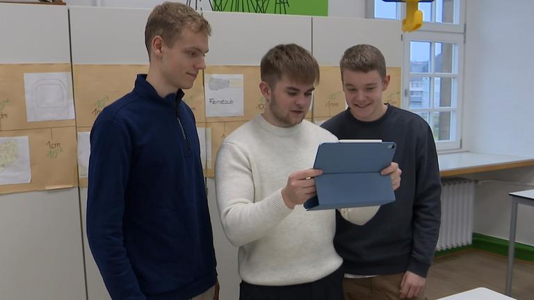 Drei junge Männer schauen auf ein iPad