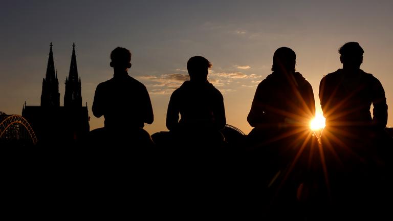Junge Männer sitzen am Rheinboulevard im Abendlicht am 26.04.2025 in Köln.
