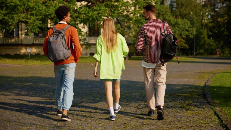 Eine Gruppe von Studierenden mit Rucksäcken geht gemeinsam auf dem Campus zum Unterricht.