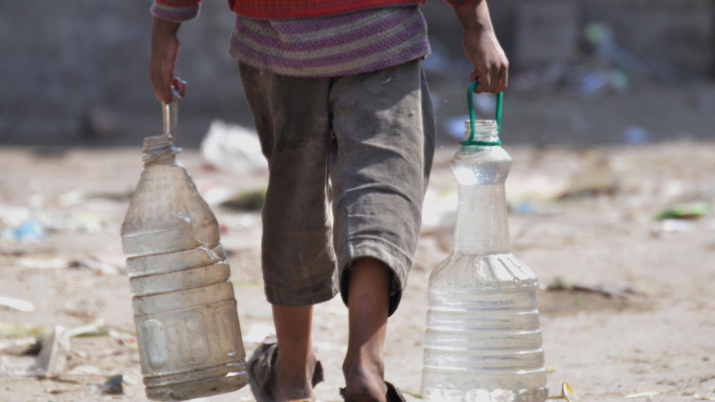 Junge wie er in beiden Händen mit Wasser gefülle Behälter trägt