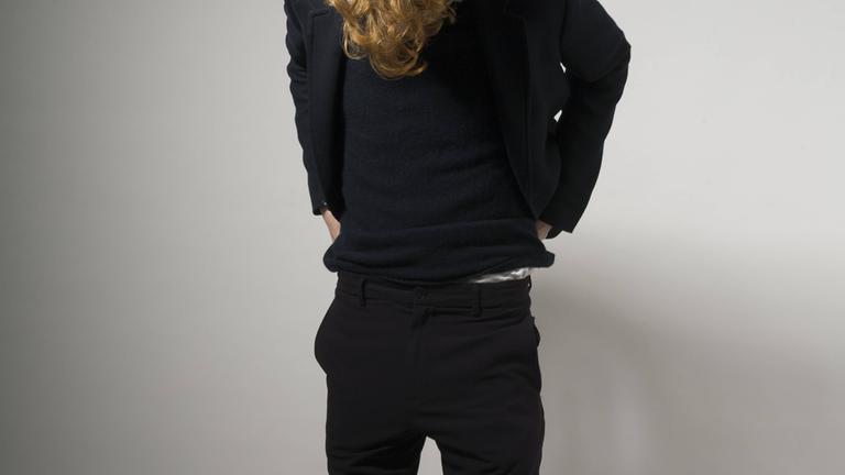 Ein junger schlanker Mann zieht sich die Hose am Bund hoch.