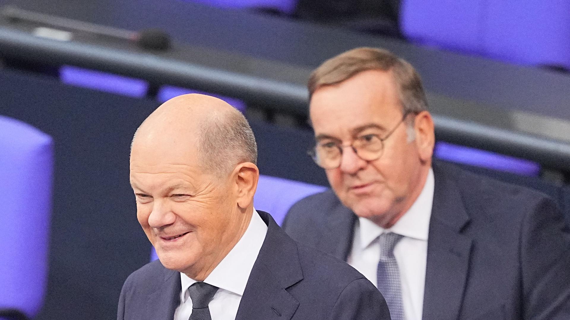 Bundeskanzler Olaf Scholz (SPD) steht lächelnd vor seiner Regierungserklärung im Plenum des Bundestags vor Boris Pistorius (SPD), Bundesminister der Verteidigung.