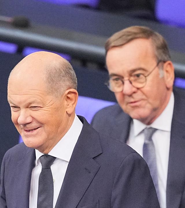 Bundeskanzler Olaf Scholz (SPD) steht lächelnd vor seiner Regierungserklärung im Plenum des Bundestags vor Boris Pistorius (SPD), Bundesminister der Verteidigung.