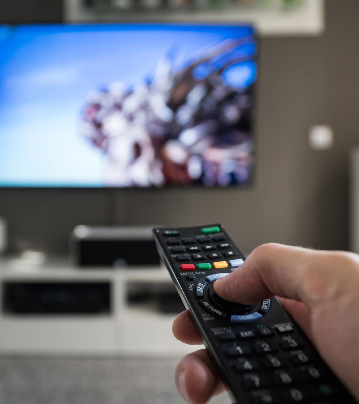 Fernbedienung in der Hand im Hintergrund Fernseher