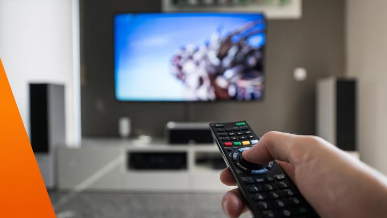 Fernbedienung in der Hand im Hintergrund Fernseher