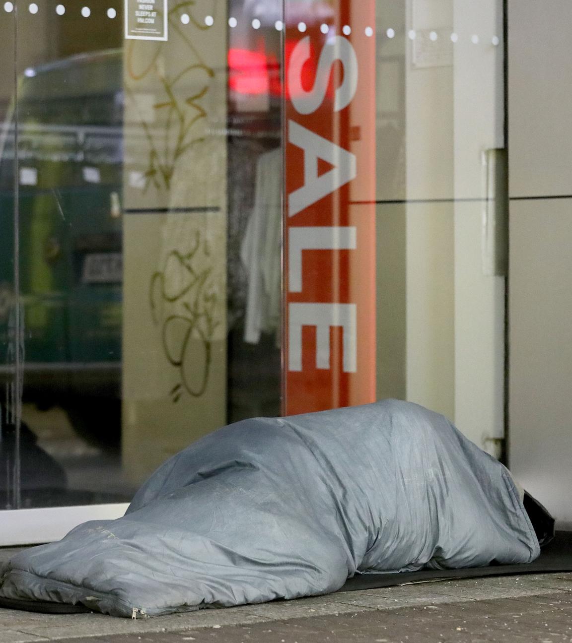 Ein Obdachloser liegt in einen Schlafsack eingewickelt in einer Fußgängerzone