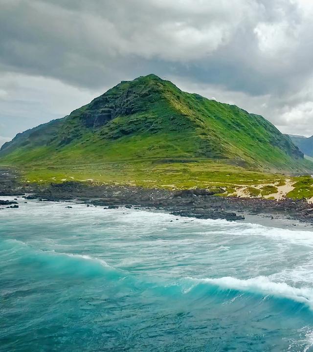 Blick auf  grünbewachsene Hügel, im Vordergrund das Meer
