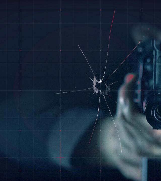 Gewehrmündung neben einem Einschussloch in der Scheibe
