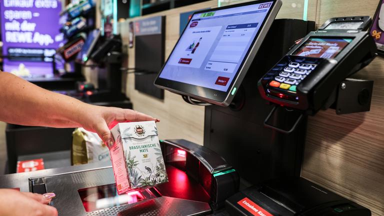 Eine Frau scannt  ein Produkt an einer Selbstbedienungskasse. 