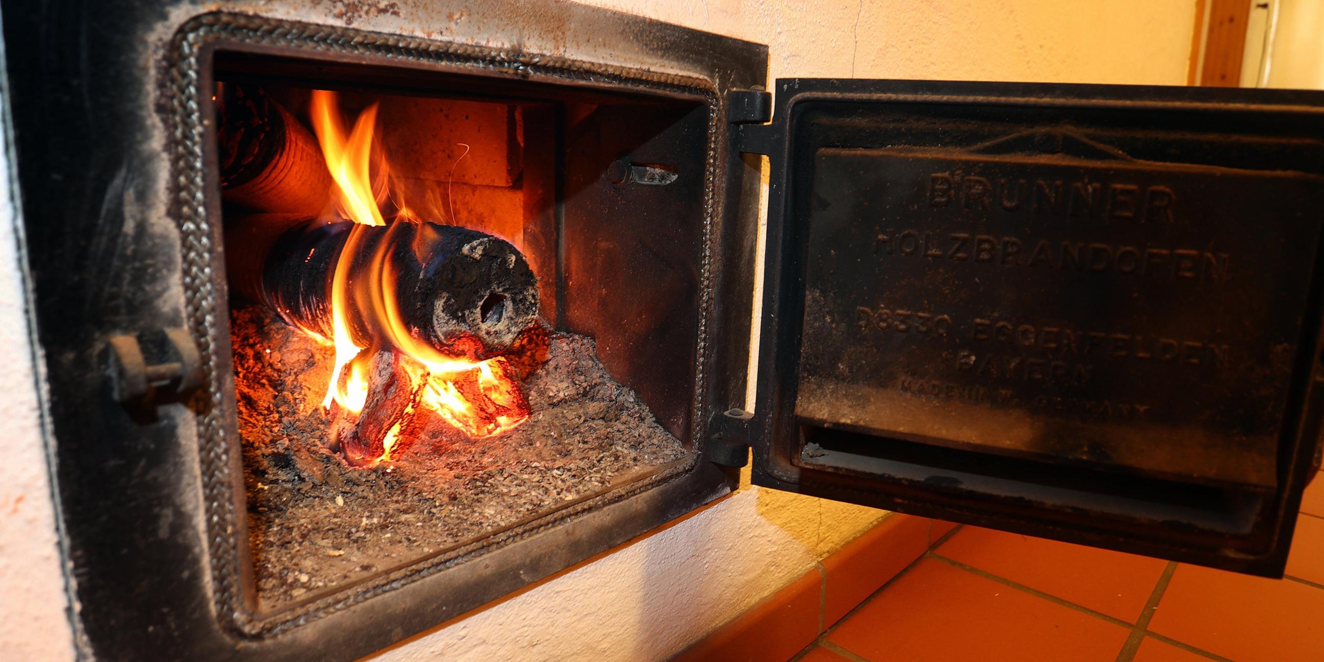 Ein Holzofen wird vom Hausflur aus mit Holzbriketts geheizt.