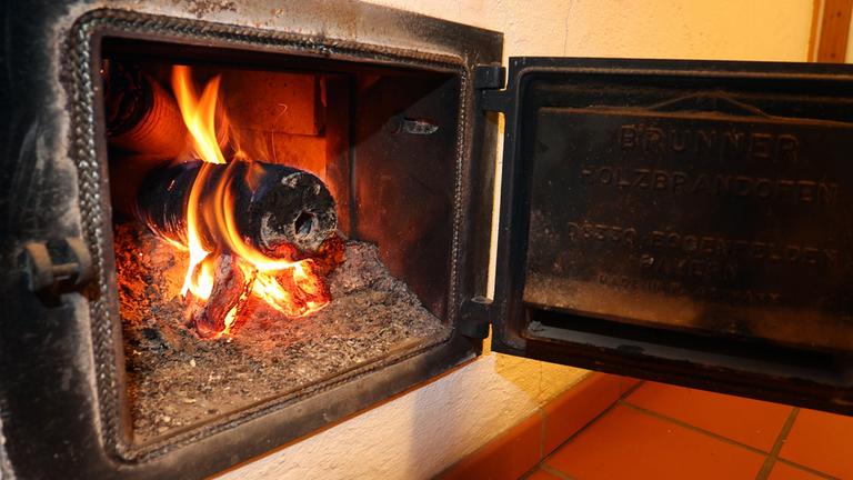 Ein Holzofen wird vom Hausflur aus mit Holzbriketts geheizt.