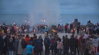 Menschen mit Fackeln stehen in einem Kreis am Kap Kolka