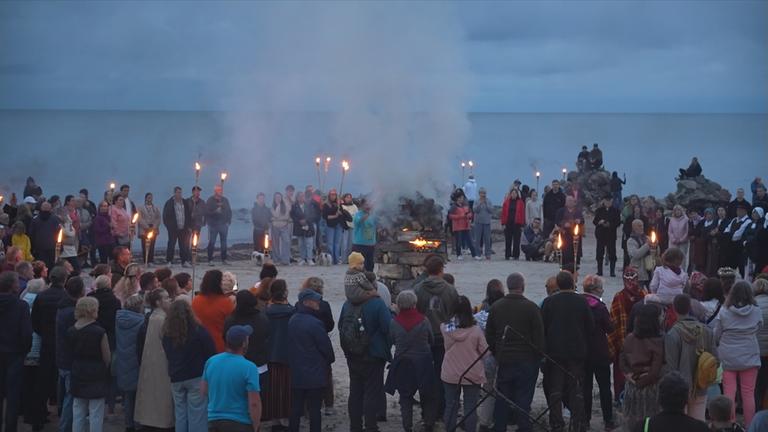 Menschen mit Fackeln stehen in einem Kreis am Kap Kolka