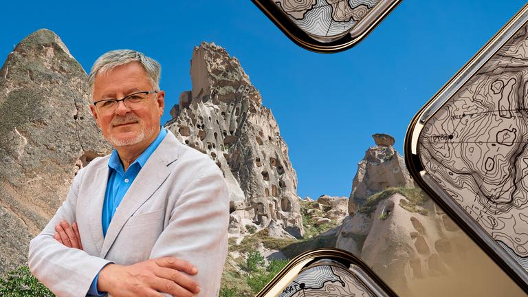 Christopher Clark vor blauem Himmel und Felsen, die Löcher haben. Sie dienen den Menschen seit Jahrhunderten als Behausung.