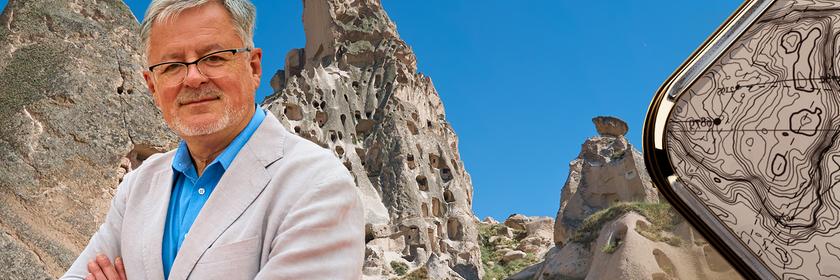 Christopher Clark vor blauem Himmel und Felsen, die Löcher haben. Sie dienen den Menschen seit Jahrhunderten als Behausung.