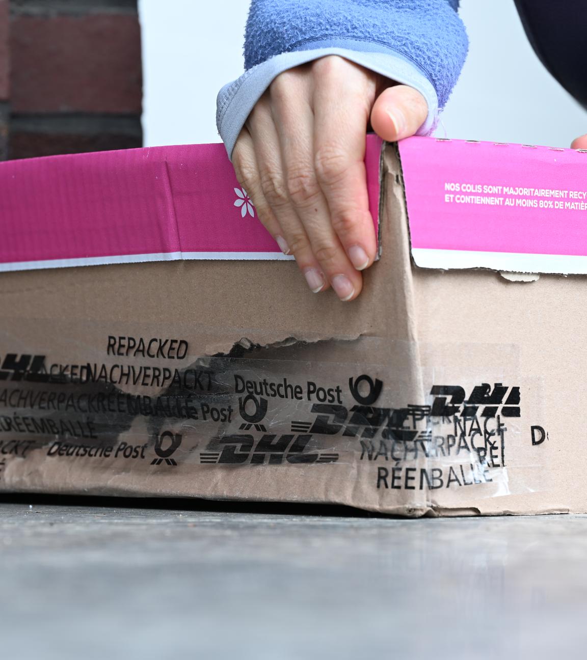 Eine Frau nimmt ein beschädigtes Paket hoch, das vor ihrer Haustür liegt.