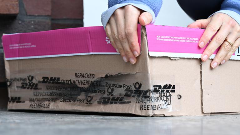 Eine Frau nimmt ein beschädigtes Paket hoch, das vor ihrer Haustür liegt.