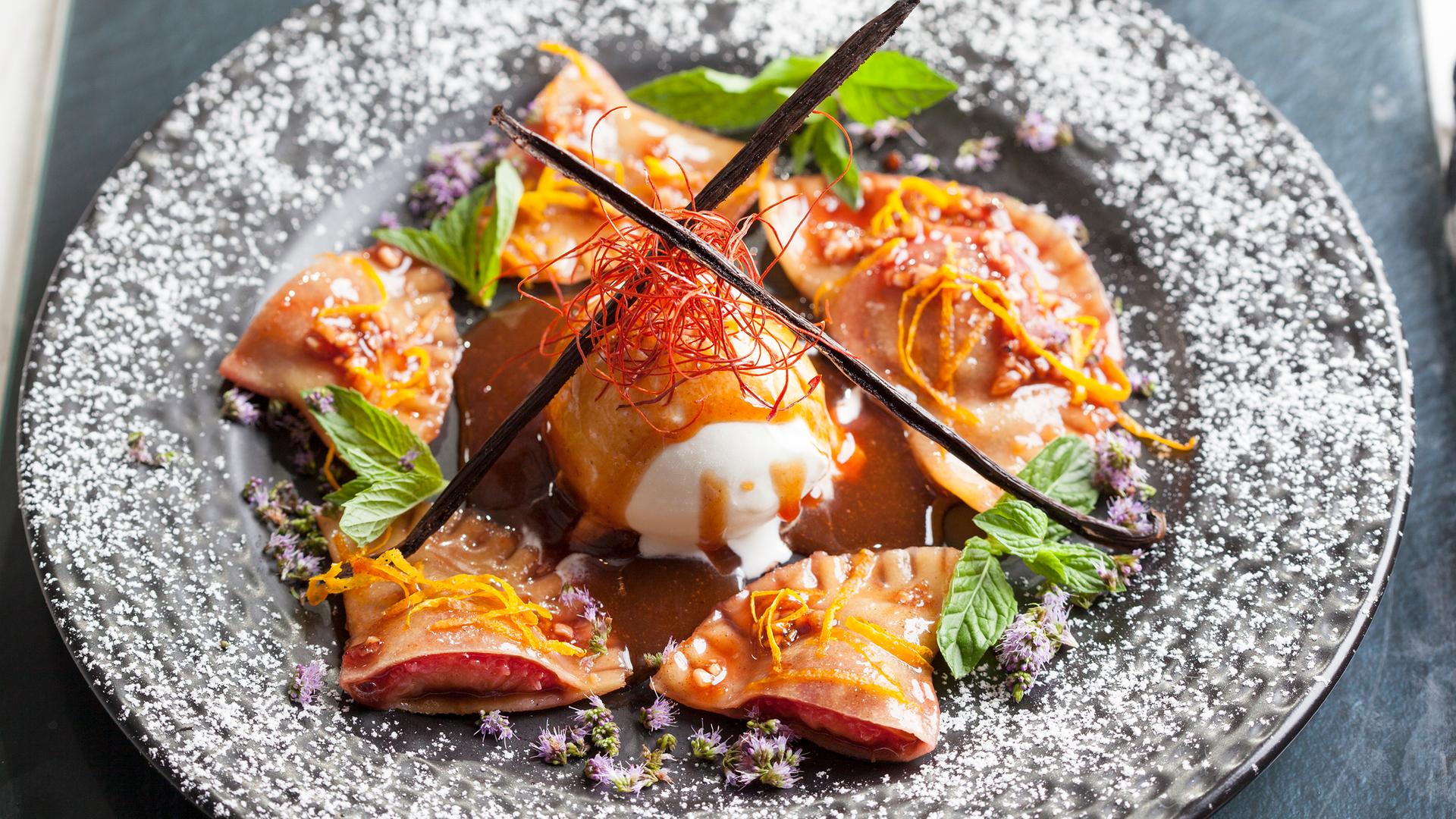 Karamellisierte Zwetschgenravioli mit Vanilleeis und Pflaumensoße in tiefem Teller angerichtet